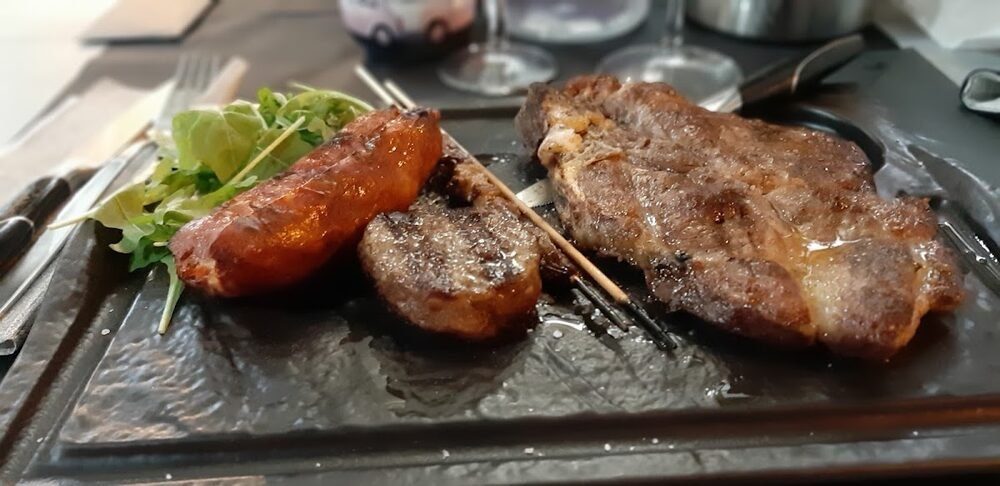 Salsiccia, fegatello e una fetta di carne alla brace serviti su ardesia con un ciuffo di insalata.